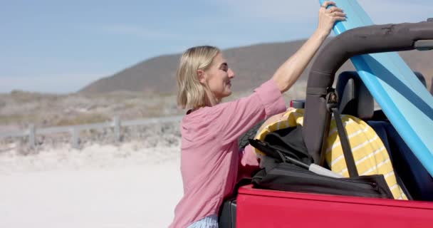 若い白人女性はコピースペース付きのロード旅行でビーチ旅行のために車をパックします 彼女の陽気なDemeanorは屋外の冒険 ゆっくりとした動きのための興奮を示唆しています — ストック動画