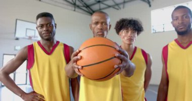 Çeşitli basketbol takımları spor salonunda güven içinde poz veriyor. Sarı formalı sporcular sahada takım çalışması ve azim sergiliyor..
