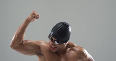 Yüzme şapkası ve gözlüklerle zaferi kutlayan bir sporcu. İfadesi ve duruşu zaferi ve rekabetçi sporların yoğunluğunu, ağır çekim.