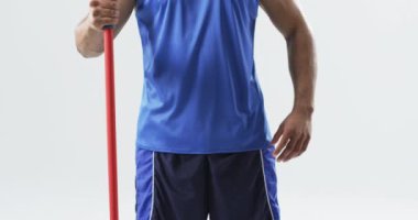 Beyaz arka planda mızrak tutan melez bir sporcu. Evde vücut geliştirme rutini, dayanıklılık eğitimi ve kendini geliştirme, yavaş çekim gösteriyor.