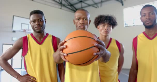 多様なバスケットボールチームがジムで自信を持ってポーズします 黄色いジャージのアスリートは 裁判所のチームワークと決意を示し スローモーション — ストック動画