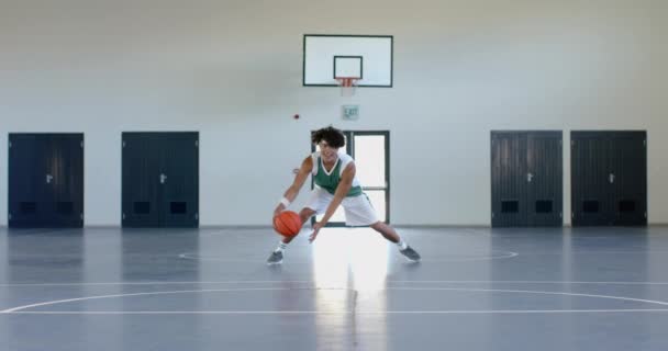 若い男は屋内裁判所でバスケットボールをする 彼のダイナミックなドリブルは 学校のジムでスキルと運動を紹介しています スローモーション — ストック動画