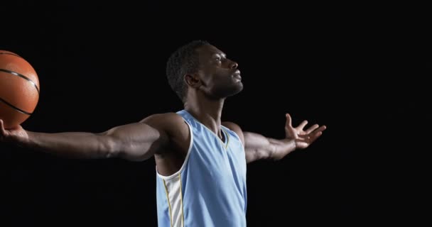 アフリカ系アメリカ人男性は 黒い背景でバスケットボールの裁判所に自信を持ってポーズします バスケットボールのショーケースのスキルとスポーツの情熱とスローモーションで彼の外側の腕 — ストック動画