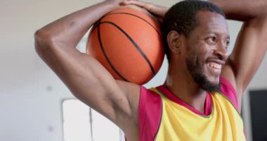 Afrikalı Amerikalı bir adam spor salonunda basketbol topuyla poz veriyor. Neşeli ifadesi spor ve fiziksel zindelik tutkusunu aktarıyor, yavaş çekim..