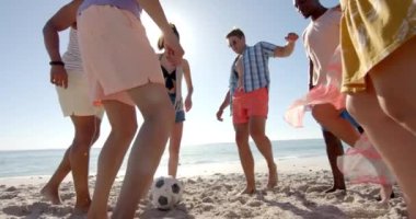 Çeşitli arkadaşlar güneşli bir plajda futbol oynarlar. Grup açık hava ortamında canlı bir oyun oynuyor, takım çalışması ve eğlence, yavaş çekim..