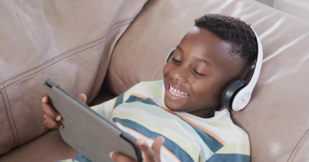 非裔美国男孩喜欢在家里用平板电脑进行数字娱乐 他沉迷于平板电脑和耳机 体验着科技的喜悦和慢动作 — 图库视频影像