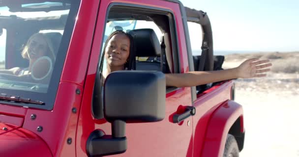 若いアフリカ系アメリカ人女性は 道路旅行で赤いジープに乗って楽しんでいます 彼女の腕は伸び 彼女は晴れた日 ゆっくりとした動きで屋外旅行の喜びを体験します — ストック動画