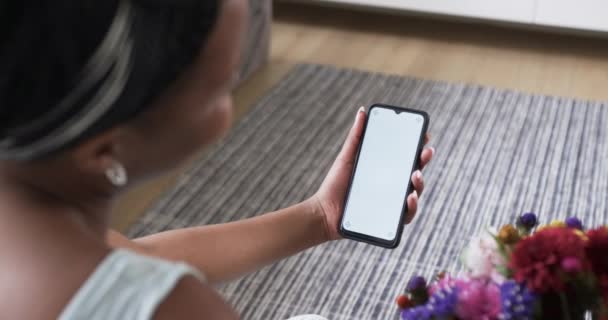若いアフリカ系アメリカ人女性が自宅にスマートフォンを持ち コピースペースがある 彼女はブラウジングしているか 空白の画面をタップする準備ができています スローモーション — ストック動画