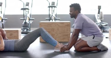 Formda beyaz bir kadın ve Afrikalı Amerikalı bir erkek spor salonunda ilaç topuyla egzersiz yapıyor. Vücut geliştirme, dayanıklılık ve takım çalışması üzerine yoğunlaşmışlar, yavaş çekim..