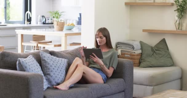 中年白人妇女在家里享受闲暇时间 并有复制空间 她躺在沙发上休息 在舒适的客厅里放着平板电脑 动作缓慢 — 图库视频影像