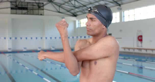 若い男性アスリート水泳選手は泳ぐ前に伸びています 彼は屋内プールにいて トレーニングや競技 スローモーションの準備をしている — ストック動画