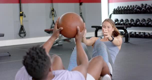 让年轻的白人女子和非洲裔美国男子在体育馆用药球做运动 他们专注于伴侣的日常锻炼 增强健康和团队精神 慢动作 — 图库视频影像