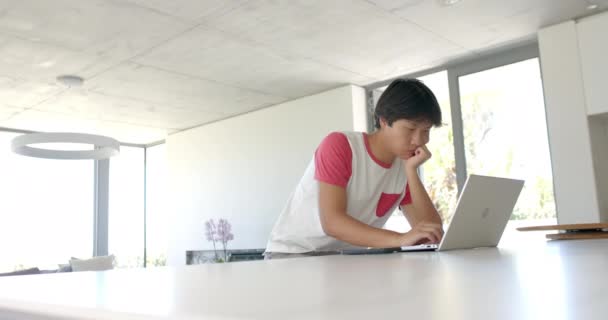 コピースペースのある自宅のオフィスで意図的に勉強している十代のアジアの少年 彼はラップトップに焦点を当て 学習や学校の仕事を完了するための献身を示唆しています スローモーション — ストック動画