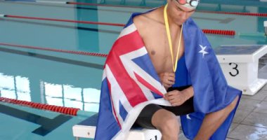 Gururlu yüzücü madalyasını bir Avustralya bayrağıyla, fotokopi alanı ile sergiliyor. Zaferini kapalı bir yüzme tesisinde, ağır çekimde kutluyor..