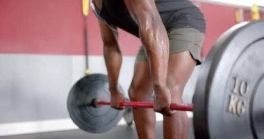 Spor salonunda ağırlık kaldıran Afro-Amerikan bir adam. Ağırdan alarak kaldırma egzersizi yaptığı için odaklanması ve gücü çok açık..