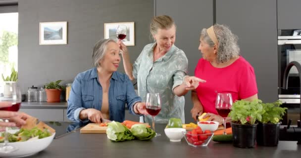 白人女性 アジア人女性 シニア女性は 食事の準備をする家庭料理セッションを楽しんでいます 彼らは新鮮な食材で満たされた台所で笑いとワインを共有し ゆっくりとした動き — ストック動画