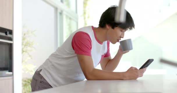 Teenage Asiatico Ragazzo Sorseggia Caffè Controlla Suo Telefono Casa Cucina — Video Stock