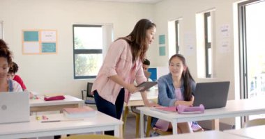 Genç melez öğretmen, lisede parlak bir sınıf ortamında Asyalı genç bir kıza yardım ediyor. Destekleyici eğitimin ve ağır çekimin önemini vurgulayan bir göreve odaklanırlar..