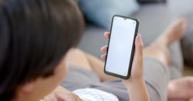 Asyalı genç çocuk evde akıllı telefon kullanıyor, fotokopi alanı da var. İnternette geziniyor ya da sosyal medyaya takılıyor, ağır çekimde..