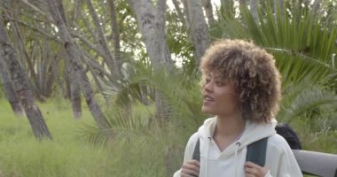 Kıvırcık saçlı melez bir kadın ormanın içinde fotokopi çekerek gülümsüyor. Beyaz bir kapüşonlu ve sırtında bir sırt çantasıyla doğa yürüyüşünden memnun görünüyor, ağır çekimde..