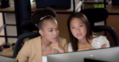 Genç Afrikalı Amerikalı kadın ve melez kadın bir iş ofisinde işbirliği yapıyorlar. Bir göreve odaklanırlar, profesyonel bir ortamda takım çalışması, yavaş çekim..