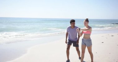 Genç bir çift ırklı adam ve beyaz bir kadın, güneşli bir sahilde fotokopi aletiyle koşuyorlar..