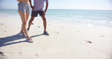 Kafkasyalı genç bir kadın, güneşli bir plajda fotokopi alanı olan melez bir genç adamın yanında akıllı bakışlarını kontrol ediyor. İkisi de spor kıyafeti giymiş. Bu da deniz kenarında ağır çekimde egzersiz yapıldığını gösteriyor..