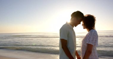 Çift ırklı çift gün batımında plaja yakın durur, alınları birbirine sevgiyle dokunur, fotokopi alanı ile. Altın ışıkla aydınlatılır, deniz kenarında sakin ve romantik bir atmosfer yaratırlar..