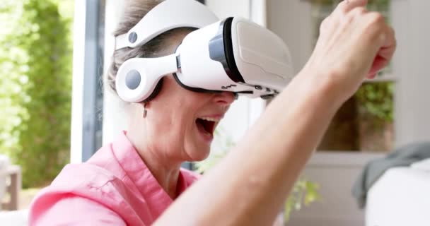 上級白人女性は 広く笑顔で仮想現実のヘッドセットに従事しています 彼女はピンクのシャツを着て 明るく屋内で現代技術を体験しています — ストック動画