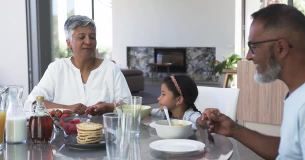 Dwurasowi Dziadkowie Jedzą Śniadanie Młodą Wnuczką Otoczoną Naleśnikami Owocami Rodzina — Wideo stockowe