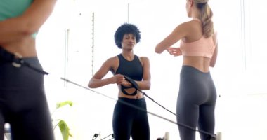 Beyaz bir kadın reformcu tarafından yönetilen direniş bantlarıyla melez kadın egzersizleri. Parlak bir çalışma alanındalar, fitness ve refahı teşvik ediyorlar, yavaş çekimde..