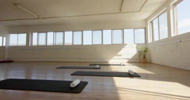 Siyah paspaslı ve beyaz destekli huzurlu bir yoga stüdyosu uygulayıcıları fotokopi alanı ile bekliyor. Güneş ışığı odayı yıkıyor, dinlenme ve egzersiz için sakin bir ortam öneriyor, ağır çekim..