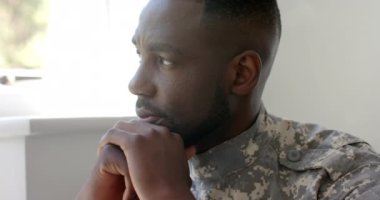 Afro-Amerikan askeri üniformalı asker evde çenesini dinlendirirken dalgın görünüyor. Pencereden dışarı bakıyor, bir anlık yalnızlığı yansıtıyor, ağır çekimde..