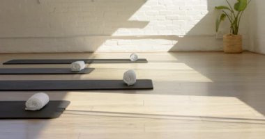 Güneş ışığı, ahşap zeminde hasırlarla dolu huzurlu bir yoga stüdyosunu fotokopi alanı ile yıkıyor. Sıcak ortam rahatlama ve meditasyon için huzurlu bir ortam olduğunu gösteriyor, yavaş çekim..