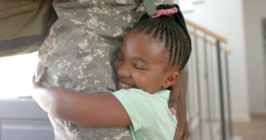 Afrikalı Amerikalı kız askeri üniformalı bir babayı kucaklıyor. Neşeli ifadesi, babasıyla yavaş çekimde, samimi bir şekilde bir araya geldiğini gösteriyor..