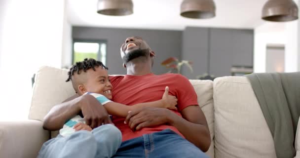非洲裔美国人和他的儿子在家里的沙发上分享着快乐的时光 两人都面带微笑 在舒适的家庭环境中表现出温馨的家庭情谊 动作缓慢 — 图库视频影像