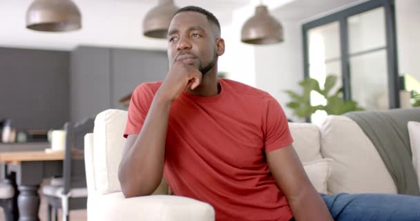 Homem Afro Americano Com Uma Camisa Vermelha Senta Pensativamente Sofá — Vídeo de Stock