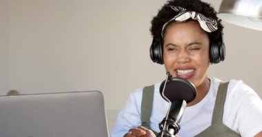 Evinde mikrofonu olan Afrikalı Amerikalı bir kadın podcast yapıyor. Kulaklık takıyor ve mikrofona konuşuyor. Podcast ya da canlı yayın yapıyor. Yavaş çekim..