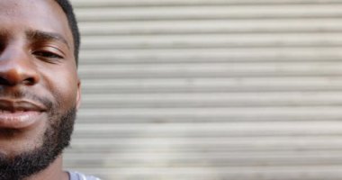 Gülümseyen, sakallı, fotokopi alanı olan genç bir Afrikalı Amerikalı 'nın yakın çekimi. Bulanık çizgili arka plana karşı kendine güveni tam. Neşeli tavrını vurguluyor. Yavaş çekim..