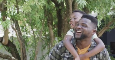 Parlak bir gülümsemesi olan Afrikalı Amerikalı bir baba sırtında neşeli bir oğul taşıyor. Yeşilliklerle çevrili bu baba ve oğul açık havada mutlu bir anı paylaşıyorlar, ağır çekimde..
