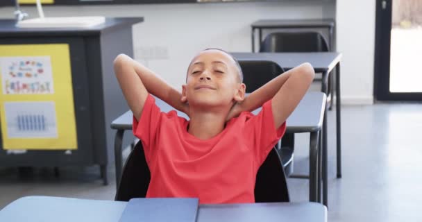 Biracial Boy Shaved Head Wearing Red Shirt Relaxes Classroom School — Stock Video