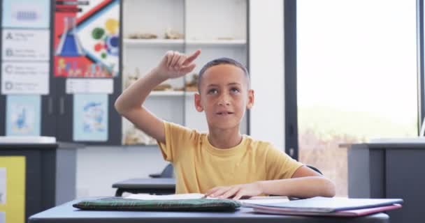 教室で平等な少年が手を挙げて 学校で質問に答えようとした 彼はノートブックを持って机に座り 学校時間中に学習環境を伝える スローモーション — ストック動画