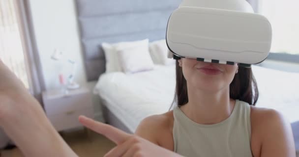 茶色の髪を持つ十代の白人少女は 家庭で仮想現実のヘッドセットを使用しています 彼女は明るく 屋内で ゆっくりとした動きでVrシミュレーションを体験して アウトリーチしています — ストック動画