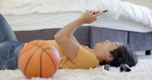 Tonårspojken Gul Skjorta Använder Smartphone När Han Ligger Golvet Basket — Stockvideo