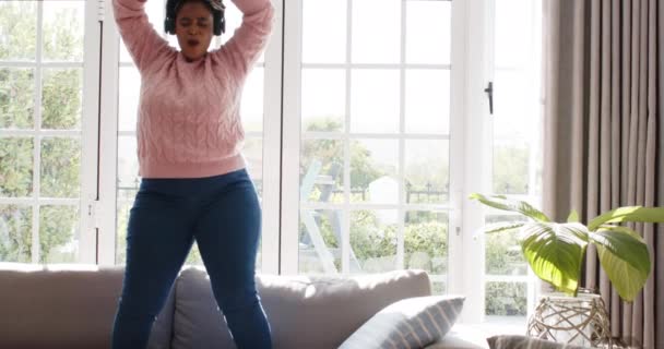 非洲裔美国妇女在室内欢快地跳舞 家里也有复制空间 她伸出双臂 在明亮的植物装饰的生活空间里 缓慢地运动着 表达着幸福 — 图库视频影像