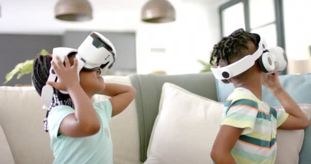 アフリカ系アメリカ人の姉妹と兄弟は 家庭で仮想現実のヘッドセットに取り組んでいます 彼らはソファーに座って 明るいリビングルームで一緒にデジタル世界を探検し スローモーション — ストック動画