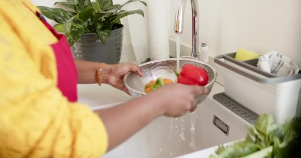 アフリカ系アメリカ人女性が 自宅でキッチンシンクでコランダーで野菜を洗う 黄色いトップを着て 彼女は明るく整頓されたキッチンセッティング ゆっくりとした動きで食べ物を準備します — ストック動画