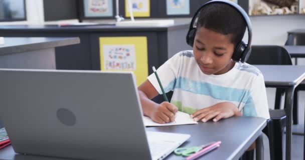 Kulaklıklı Melez Çocuk Dizüstü Bilgisayar Kullanıyor Okuldaki Bir Sınıfta Notlar — Stok video