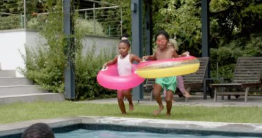 Afrika kökenli Amerikalı kardeşler babalarına yüzme havuzuna atlıyorlar. Açık hava ayarı eğlenceli bir anı yakalar, aile bağlarını ve boş zamanlarını vurgular, yavaş çekim.