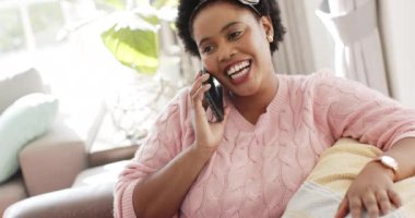 Afro-Amerikalı kadın telefonda konuşuyor, evde şaşkınlığını dile getiriyor. İçeride oturmuş, pembe bir kazak ve saç bandı takmış, canlı bir sohbete dalmış, ağır çekimde..